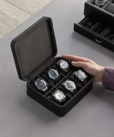 A person's hand holds the Fraser 6 Watch Case - Black by TAWBURY, a luxurious leather storage solution housing six wristwatches of various designs.